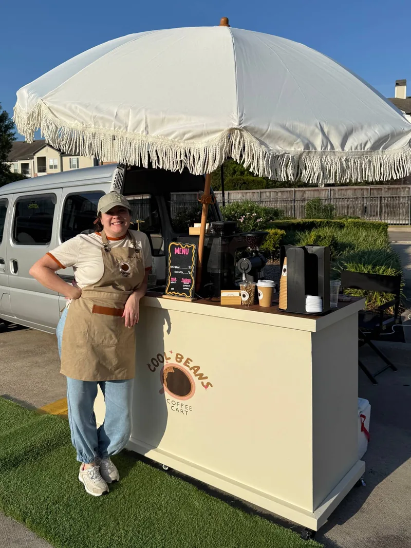 Makayla with the Cool Beans cart under its fringe umbrella at an outdoor setup