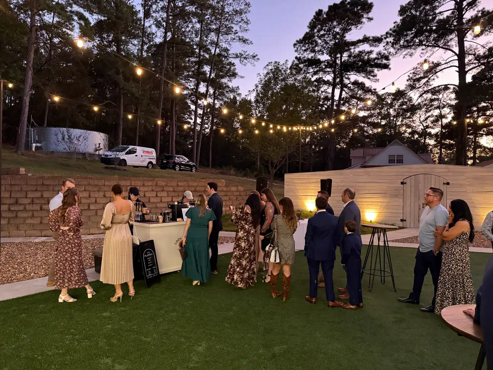 Guests gathering around the Cool Beans mobile coffee cart at an outdoor evening wedding reception under string lights